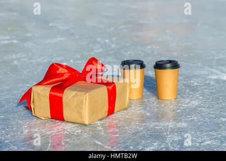 Cadeaux artisanat avec ruban rouge et tasses de café sur la patinoire. Banque D'Images