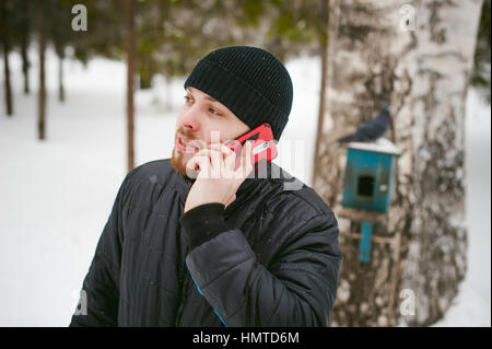Un jeune homme avec une barbe, fume une cigarette électronique et un plaisir de parler au téléphone par Internet, un effet positif de détente en plein air dans le sn Banque D'Images