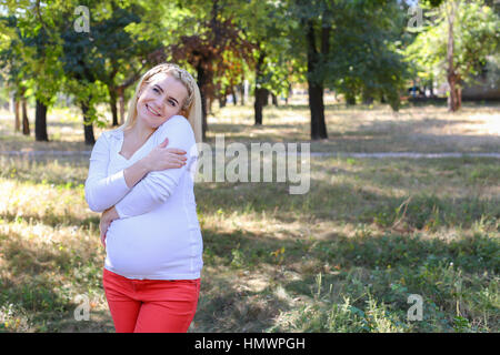 Belle Femme et future mère prépare pour la naissance de bébé, fatigué et essayer de se détendre, se faisant passer pour des photos sur la mémoire et se trouve dans le parc ensoleillé vert Outdo Banque D'Images