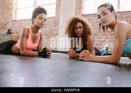 Portrait de trois jeunes femmes se trouvant sur plancher du gymnase et à la recherche à l'appareil photo. Les femelles en cours de conditionnement physique. Banque D'Images