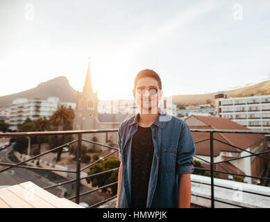 Portrait de beau jeune homme debout sur le toit. Portrait jeune homme portant des lunettes de soleil sur la terrasse à la caméra et au sourire. Banque D'Images