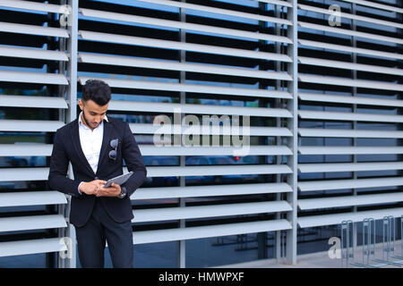 Young handsome businessman musulmans arabes est dans le centre d'affaires en noir élégante robe sur la construction de l'arrière-plan. L'homme d'affaires homme désirant en attente Banque D'Images