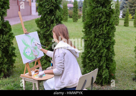 Assez intéressant artiste commence à la peinture qui illustre, papillon coloré assis avec retour au photographe et derrière de chevalet, détient, palette Banque D'Images