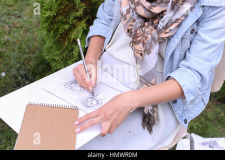 Jeune femme talentueuse gère les détails, obscurcit les cheveux en photo. Exécution de croquis au crayon ordinaire sur la feuille de papier graphique, qui allongé sur sol en bois Banque D'Images