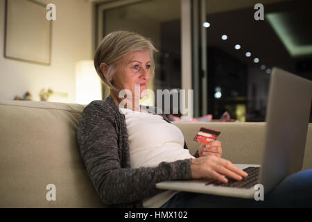 Senior woman with laptop sitting on the couch shopping online Banque D'Images