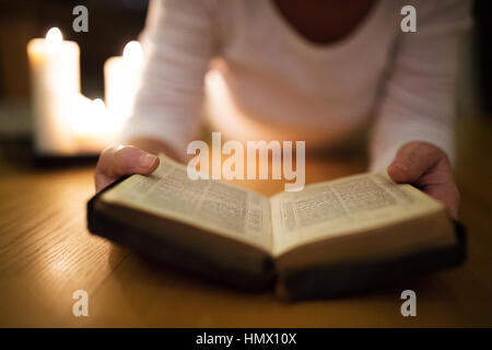 Méconnaissable woman reading Bible. Brûler des bougies à côté d'elle. Banque D'Images