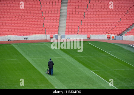 Homme seul coupe le gazon dans un grand vide, stade de football. Banque D'Images