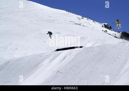 Snowboarder et skieur sautant dans parc de neige à ski sur journée d'hiver ensoleillée. Montagnes du Caucase, région Chelyabinsk. Banque D'Images