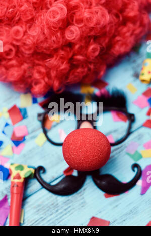 Une perruque rouge, une paire de lunettes noires avec de faux sourcils, un nez de clown rouge et une moustache formant la face d'un homme sur une surface en bois rustique bleue pleine Banque D'Images