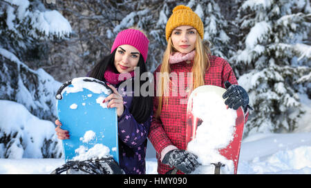 Deux filles attirantes les néviplanchistes sont parmi les sapins enneigés en hiver et garder les planches à mains, close-up portrait Banque D'Images