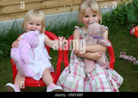 Petites filles, enfants assis sur la chaise en plastique sur le jardin jouer ensemble, serrant son ours en peluche Teddy Bears Picnic love joy l'enfance heureux Banque D'Images