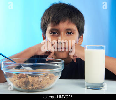 Garçon s'ennuie sur le petit-déjeuner avec du lait et des céréales s'asseoir sur la table Banque D'Images