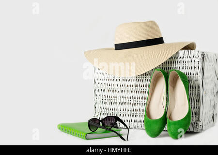 Valise en osier blanc, womens chapeau, lunettes, chaussures vert et le bloc-notes. Focus sélectif. Banque D'Images