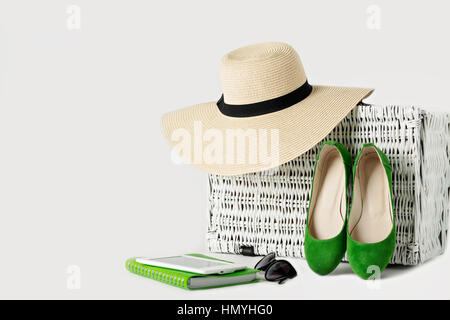 Valise en osier blanc, womens chapeau, lunettes, chaussures vert, e-book et le bloc-notes. Focus sélectif. Banque D'Images