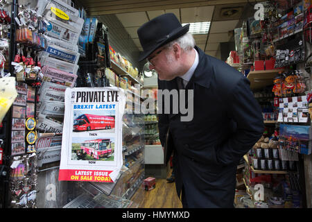 Homme portant un chapeau trilby s'arrêter pour regarder une copie de "Private Eye" magazine dans un kiosque à Londres, Victoria, England, United Kingdom Banque D'Images