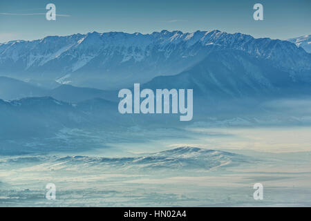 Paysage d'hiver enneigé idyllique avec Piatra Craiului de montagnes et vallées Brumeux le matin, la Roumanie. Banque D'Images