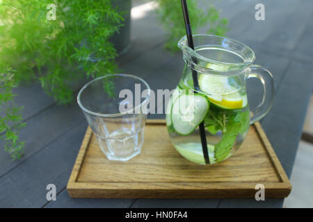 Carafe en verre noir et paille avec verre de concombre, de citron, de menthe et de verre vide coupe à facettes se dresse sur planche en bois gris sur wo Banque D'Images