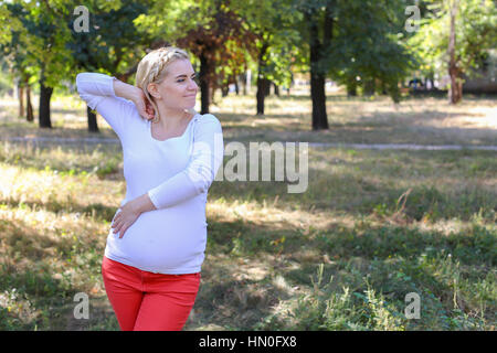 Belle Femme et future mère prépare pour la naissance de bébé, fatigué et essayer de se détendre, se faisant passer pour des photos sur la mémoire et se trouve dans le parc ensoleillé vert Outdo Banque D'Images