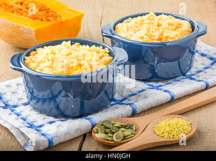 Porridge de millet avec citrouille dans bol bleu sur une serviette de cuisine, graines de citrouille et de mil dans une cuillère en bois et de citrouille sur une table en bois Banque D'Images