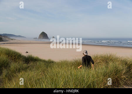 Un homme marche à travers les dunes de Cannon Beach Oregon, admirer la plage et l'emblématique Haystack Rock. Banque D'Images