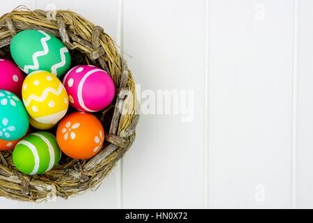 Close up d'un ressort nid rempli d'oeufs de Pâques colorés contre un arrière-plan en bois blanc Banque D'Images
