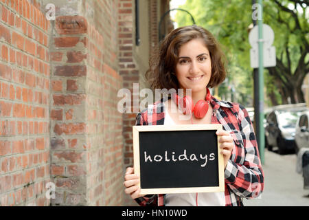 Young Beautiful woman holding tableau sur lequel un texte 'vacances'. À l'extérieur. Banque D'Images