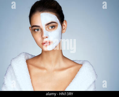 Gorgeous woman avec un masque sur son visage. Photo de belle fille brune vêtu de blanc peignoir. Concept de bien-être et spa Banque D'Images