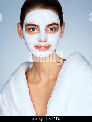 Femme souriante avec masque facial hydratant. Photo de brunette woman wearing white peignoir. Beauté et Soins De La Peau concept Banque D'Images