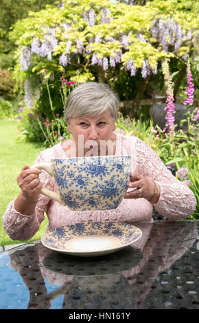 Femme à boire le thé d'une très grande Chine tasse dans un jardin Devonshire Banque D'Images