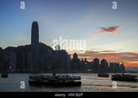 Silhouette de quatre Star Ferries, des gratte-ciel et autres bâtiments sur l'île de Hong Kong à Hong Kong, Chine, au coucher du soleil. Vue de la station de métro Tsim Sha Tsui. Banque D'Images