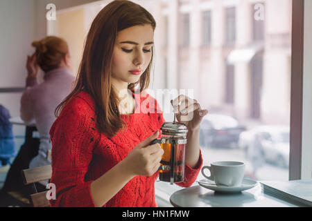 Jeune fille verse le thé noir de la vitre électrique de petite tasse à café avec grande fenêtre Banque D'Images