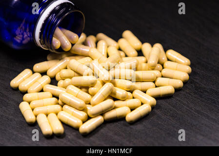 Bouteille de pilules pilules déversant sur à la surface isolée sur un fond noir Banque D'Images