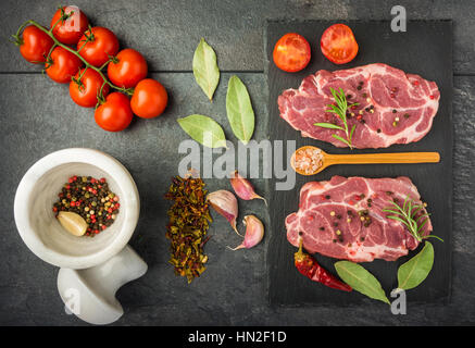 Steak de boeuf aux épices, les tomates sur un tableau sombre de la préparation vue d'en haut Banque D'Images