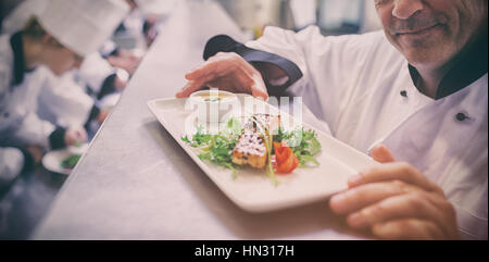 Chef cuisinier heureux avec dish with fini stagiaires travaillant dans la cuisine Banque D'Images