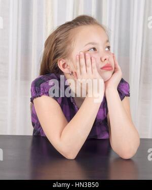 Portrait d'un enfant mignon ennuyé assis à la table Banque D'Images