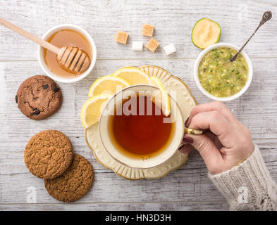 Femme à boire le thé avec du citron . les cookies, le sucre , le miel, confiture de feijoa feijoa et allongé sur une table en bois blanc. Banque D'Images