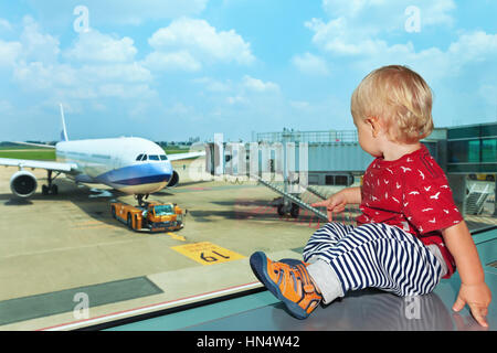 Little baby boy waiting l'embarquement à l'aéroport en vol et l'hôtel de transit à travers la fenêtre de l'avion à près de d'embarquement. Banque D'Images