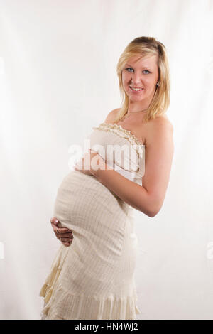 Belle jeune femme aux cheveux blonds enceinte en robe blanche Banque D'Images