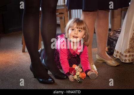 Cute little girl holding Flowers et ramper entre les jambes des invités à la réception de mariage Banque D'Images