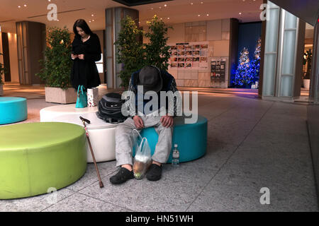 Belle japonaise woman texting on smartphone et sans-abri dormant dans le hall d'un immeuble moderne. Tokyo, Japon, Asie Banque D'Images