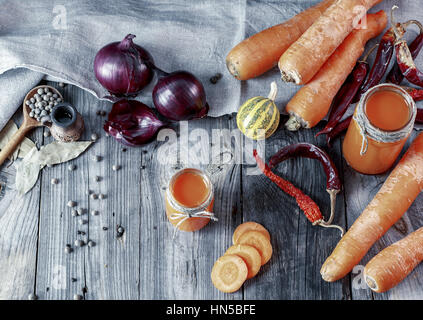 Des jus de carotte dans des bocaux en verre sur une surface en bois gris parmi les légumes et épices, vintage toning Banque D'Images