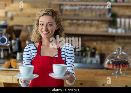 Portrait of smiling waitress offrant une tasse de café dans la région de cafÃƒÂ© Banque D'Images