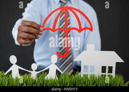 Mid section of businessman la protection de papier découpées hors famille, maison et voiture avec parapluie Banque D'Images