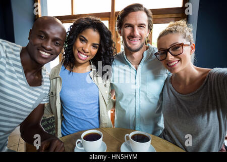 Portrait of smiling friends avec les tasses de café sur la table en cafÃƒÂ© Banque D'Images