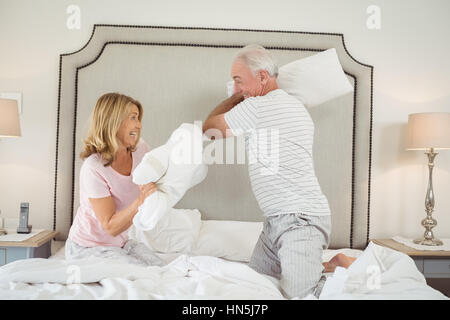 Laughing couple having pillow fight sur le lit dans la chambre Banque D'Images