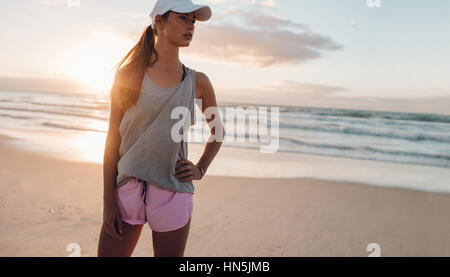 Tiré de santé de la jeune femme debout sur la plage avec sa main sur la hanche et à la voiture. Modèle féminin dans les vêtements de sport sur le bord de la mer dans la matinée. Banque D'Images