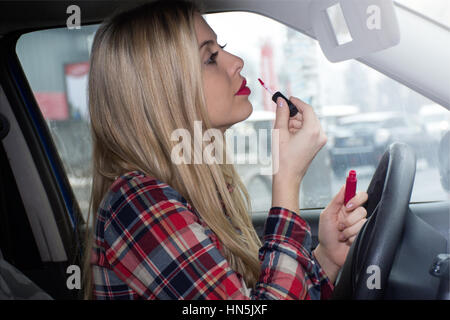 Young woman putting on lustre de lèvre dans une voiture Banque D'Images