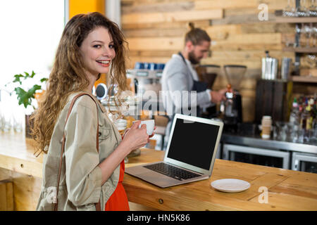 Portrait de femme debout au comptoir et à l'aide d'ordinateur portable tout en ayant le café dans cafÃƒÂ© Banque D'Images