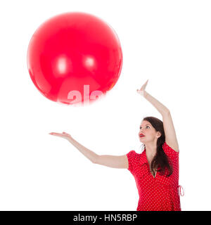 Belle femme en robe rouge de la capture d'un gros ballon rouge au-dessus de sa tête isolé sur fond blanc Banque D'Images