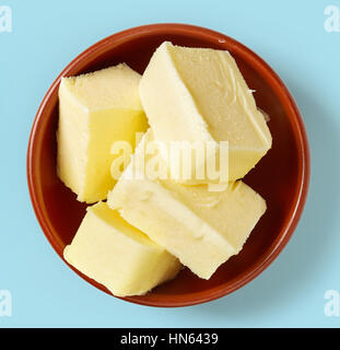Morceaux de beurre dans la cuvette d'argile sur fond bleu clair, vue du dessus Banque D'Images